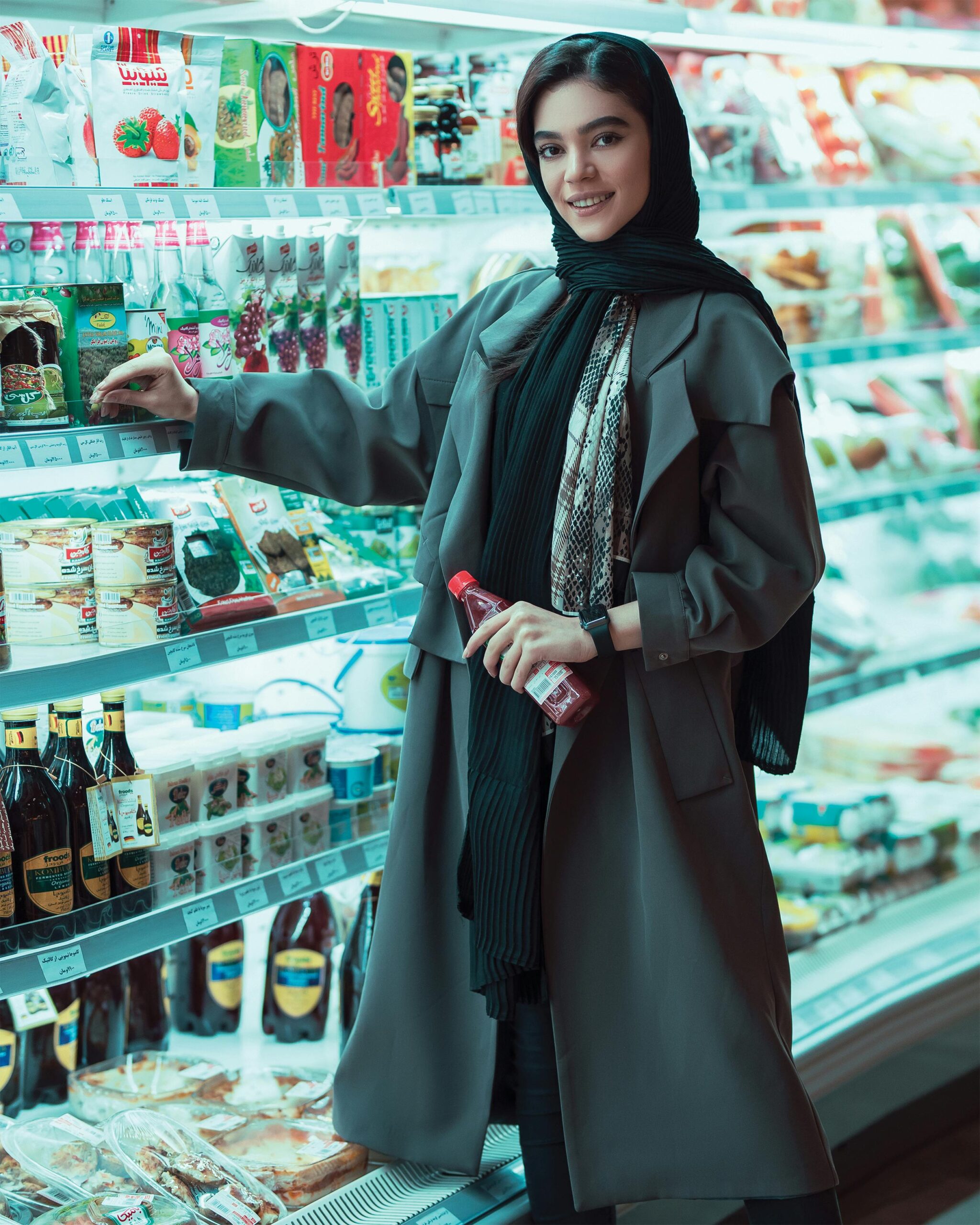 A stylish woman in a headscarf shopping in a well-lit supermarket aisle, smiling as she examines products.